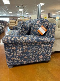 a blue and white floral couch sitting on top of a hard wood floor in a store