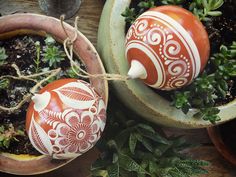 two red and white painted eggs sitting on top of potted plants