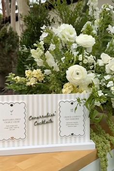 white flowers and greenery are on display in a glass case at a flower shop