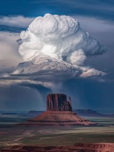 a large cloud is in the sky over a desert area with a rock formation on it