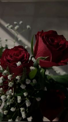 two red roses are in a vase with white baby's breath and greenery