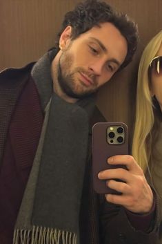 a man and woman taking a selfie in front of a wall with their cell phones