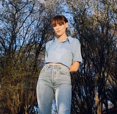 a woman standing in front of trees with her hands on her hips and looking at the camera