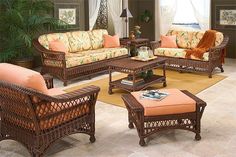 a living room with wicker furniture and orange pillows on the couches in front of a window