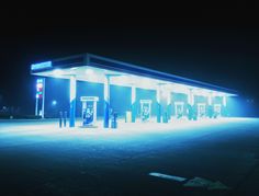 an empty gas station at night with blue lights on the front and side of the building