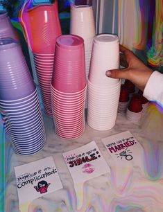 there are many different colored cups on the table and one person is pointing at them