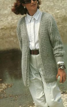 a woman walking on the beach in white pants and a gray cardigan over her shirt