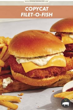 two chicken sandwiches with cheese and french fries on a cutting board next to some ketchup