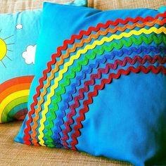 two colorful pillows sitting on top of a couch next to each other with a rainbow painted on them