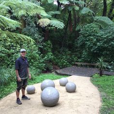 a man standing in front of some balls on a dirt path surrounded by greenery