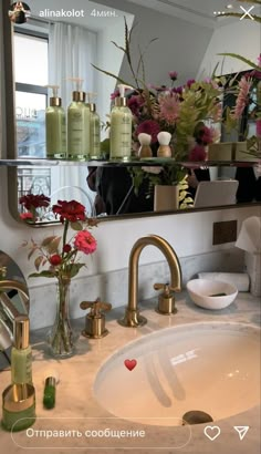 a bathroom sink sitting under a mirror next to a vase with flowers on top of it