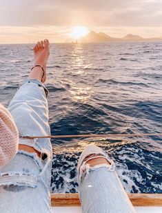 a person's feet on the edge of a boat in the ocean at sunset