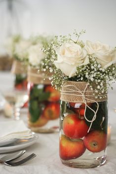 mason jar filled with apples and flowers on top of a white tablecloth covered table