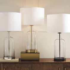 two lamps are sitting on top of a dresser next to a lamp with a white shade