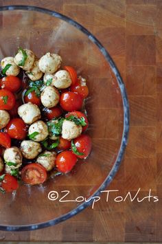 a glass bowl filled with tomatoes and cauliflower on top of a wooden table