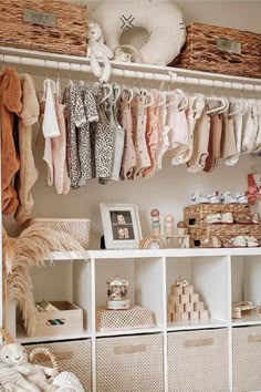 a closet filled with lots of baby clothes and baskets on top of white shelving