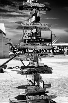 black and white photograph of a street sign post with many different signs on it's side