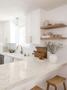 a kitchen with white cabinets and countertops has wooden stools in front of the sink