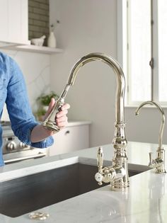 a woman washing her hands under a kitchen faucet with water running from it