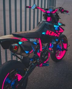 a pink and black dirt bike parked next to a fence