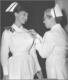 an old photo of two women dressed in nurses'uniforms, one adjusting the collar of another woman's dress