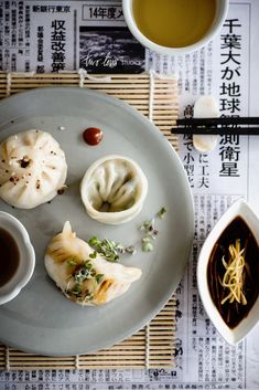 a plate topped with dumplings next to cups of tea and chopsticks on top of a table