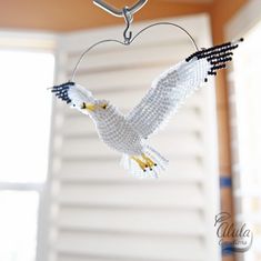 a beaded bird hanging from a hook in a room with shutters and windows