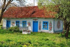 a small white house with blue doors and red tile roof, sitting in the grass