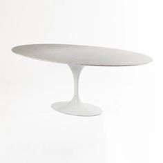 an oval dining table with a white base on a plain surface, in the shape of a tulip