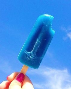 a hand holding an ice lolly with the letter l on it in front of a blue sky