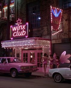 a pink car parked in front of a building with fairy wings on it's roof