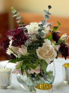 a vase filled with lots of flowers on top of a white table covered in silver cups