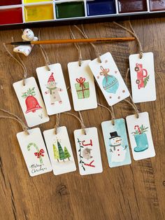 some tags are hanging on a wooden table with paintbrushes and watercolors