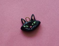 a black cat brooch with green eyes on a pink surface