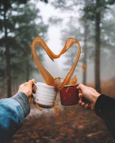 two people holding cups in the shape of a heart with liquid pouring out of them