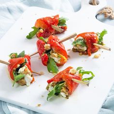 several small appetizers are arranged on a white cutting board with toothpicks