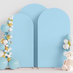 a teddy bear sitting in front of balloons on a blue background with an arch shaped like the letter i