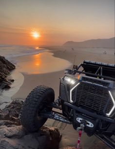 an off - road vehicle driving on the beach at sunset