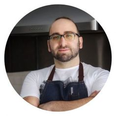 a man with glasses and an apron in front of a white background is looking at the camera