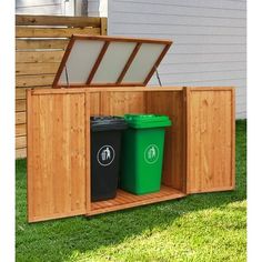 two trash cans are in the back of a wooden storage box on grass next to a house