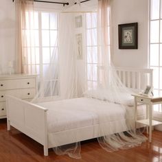 a white bed sitting in a bedroom next to a window with sheer curtains on it