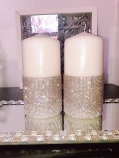 two white candles sitting next to each other on top of a table in front of a mirror