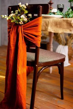 an orange sash draped over a chair with flowers on it's back and table in the background