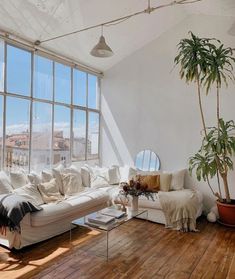 a living room filled with white furniture and large windows overlooking the cityscape in the distance