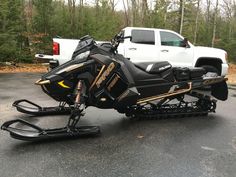 a black and gold snowmobile parked in front of a white truck