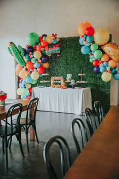 a table topped with lots of balloons next to a wall covered in green plants and cactuses