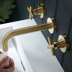 a person washing their hands under a faucet in a bathroom sink with gold fixtures