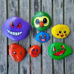 five painted rocks sitting on top of a wooden table next to each other with faces drawn on them