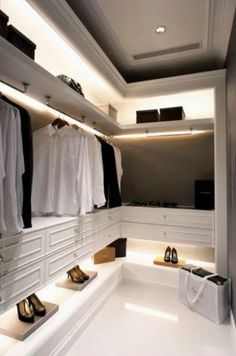 a white closet with shoes and shirts hanging on the wall, lighting up by recessed lights