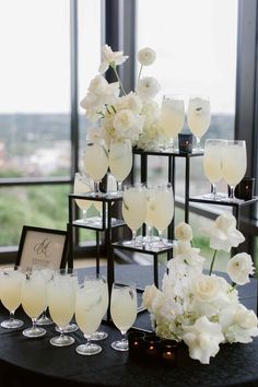 a table topped with lots of glasses filled with white flowers and wine glasses next to each other